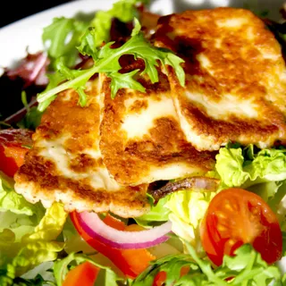 Slices of cheese grilled dark over charcoal.