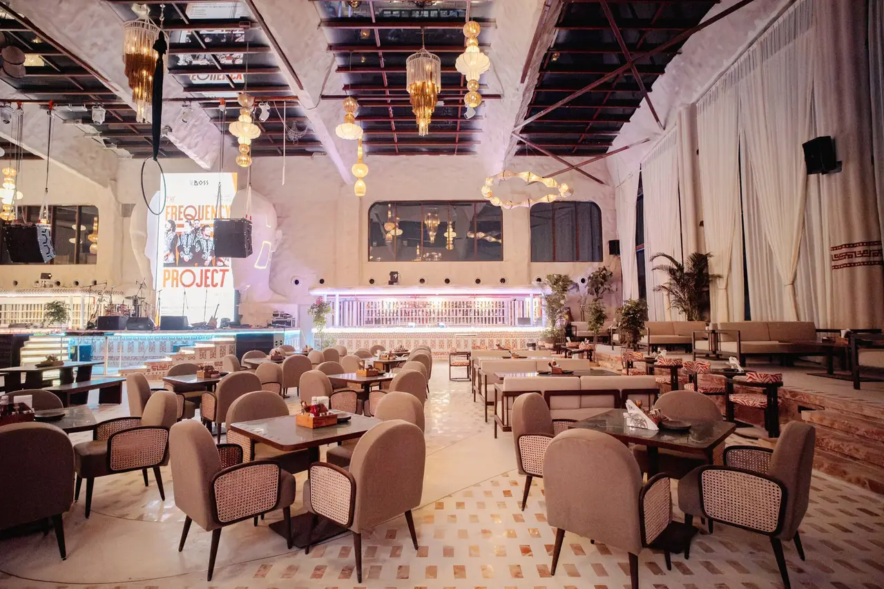 The hall with event posters standing between the tall window bays, the bar and the mezzanine rail at the far end.