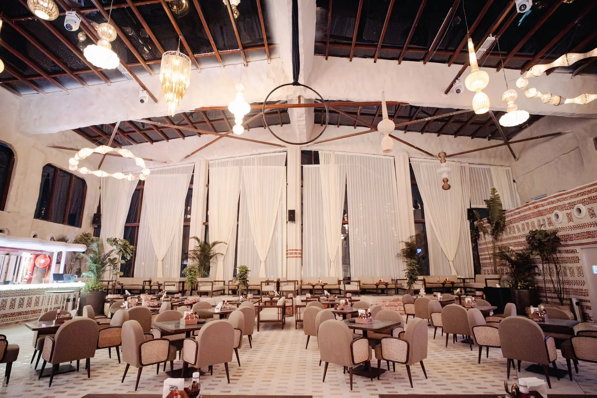 The BOSS hall from the back: rows of cane chairs and set tables under bulb chandeliers and an open timber roof, sheer drapes across the far wall.