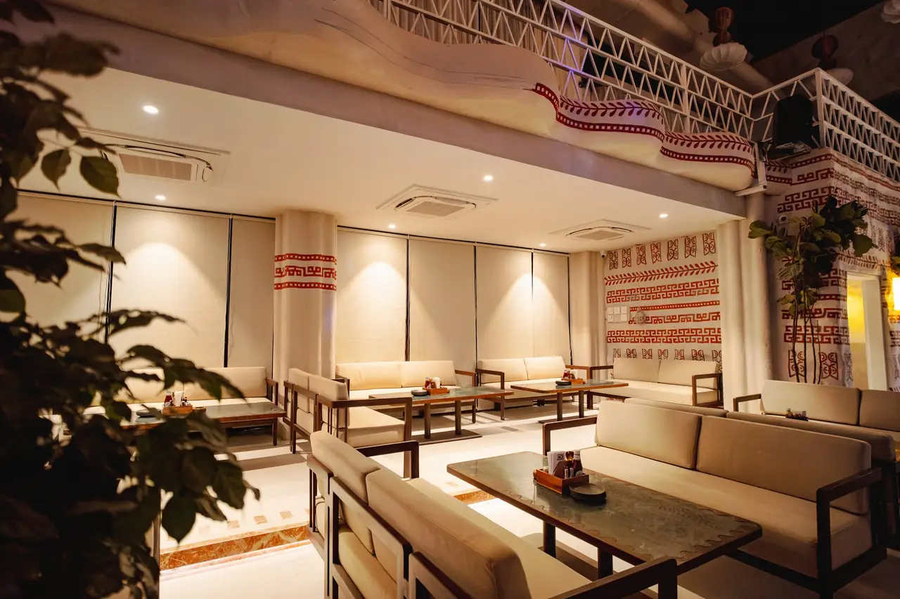 The mezzanine lounge seen past a large plant, sofas and low tables under the lattice balcony.