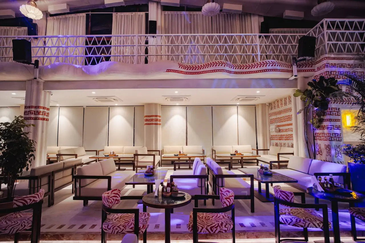 Zebra-print armchairs and white sofas in the mezzanine lounge, purple light along the lattice balcony above.