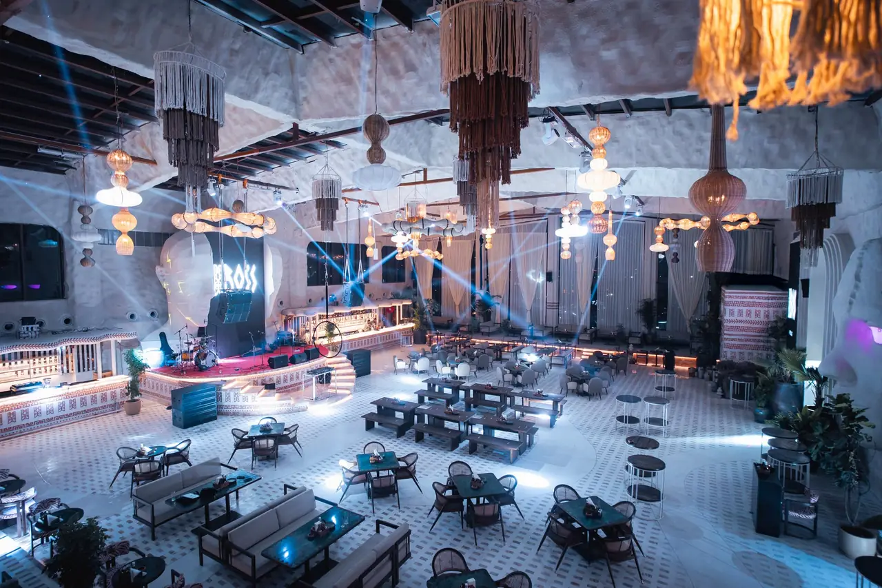 The floor at night under blue light, the BOSS sign glowing above the bar and tasselled chandeliers overhead.
